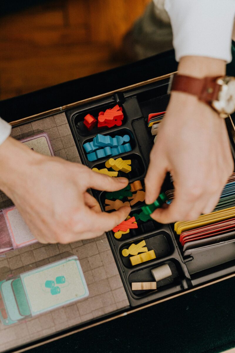 Close-up of hands organizing a board game with colorful pieces indoors.